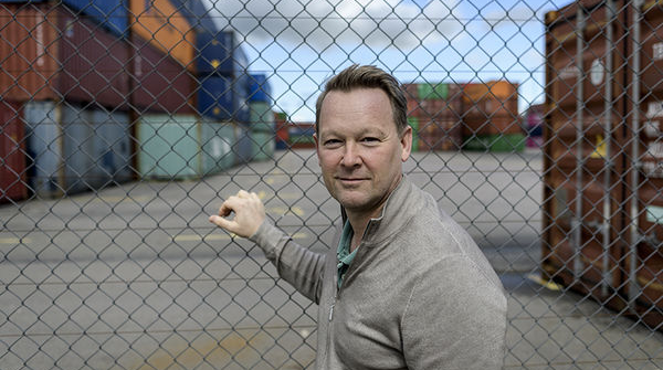 man står framför ett staket med containers i bakgrunden. Foto. 
