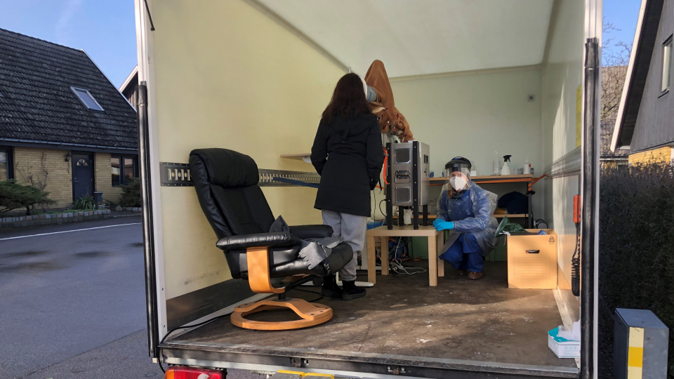 två personer står inuti en liten lastbil full av mätutrustning placerad i ett villakvarter. Foto.