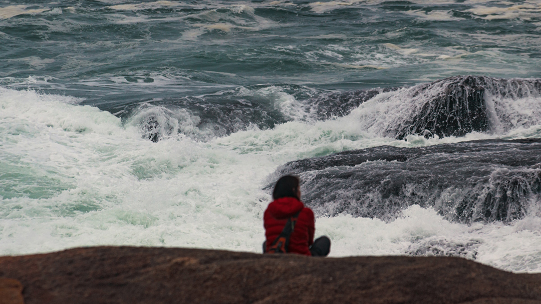 en person i förgrunden tittar ut över ett stormigt hav. Foto. 