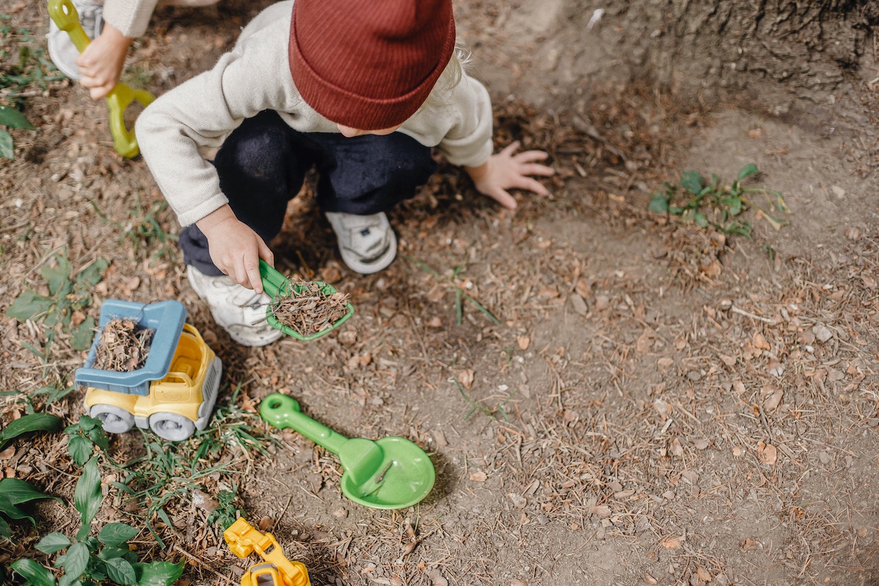 ett barn gräver med spade utomhus. Foto. 