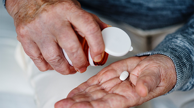 äldre person häller upp piller i handen. Foto. 