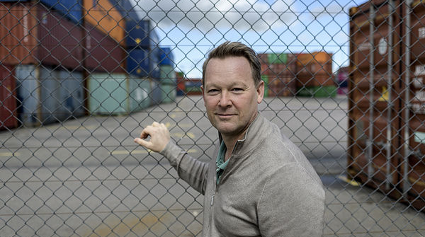 man står vid ett stängsel med containers i bakgrunden. Foto. 