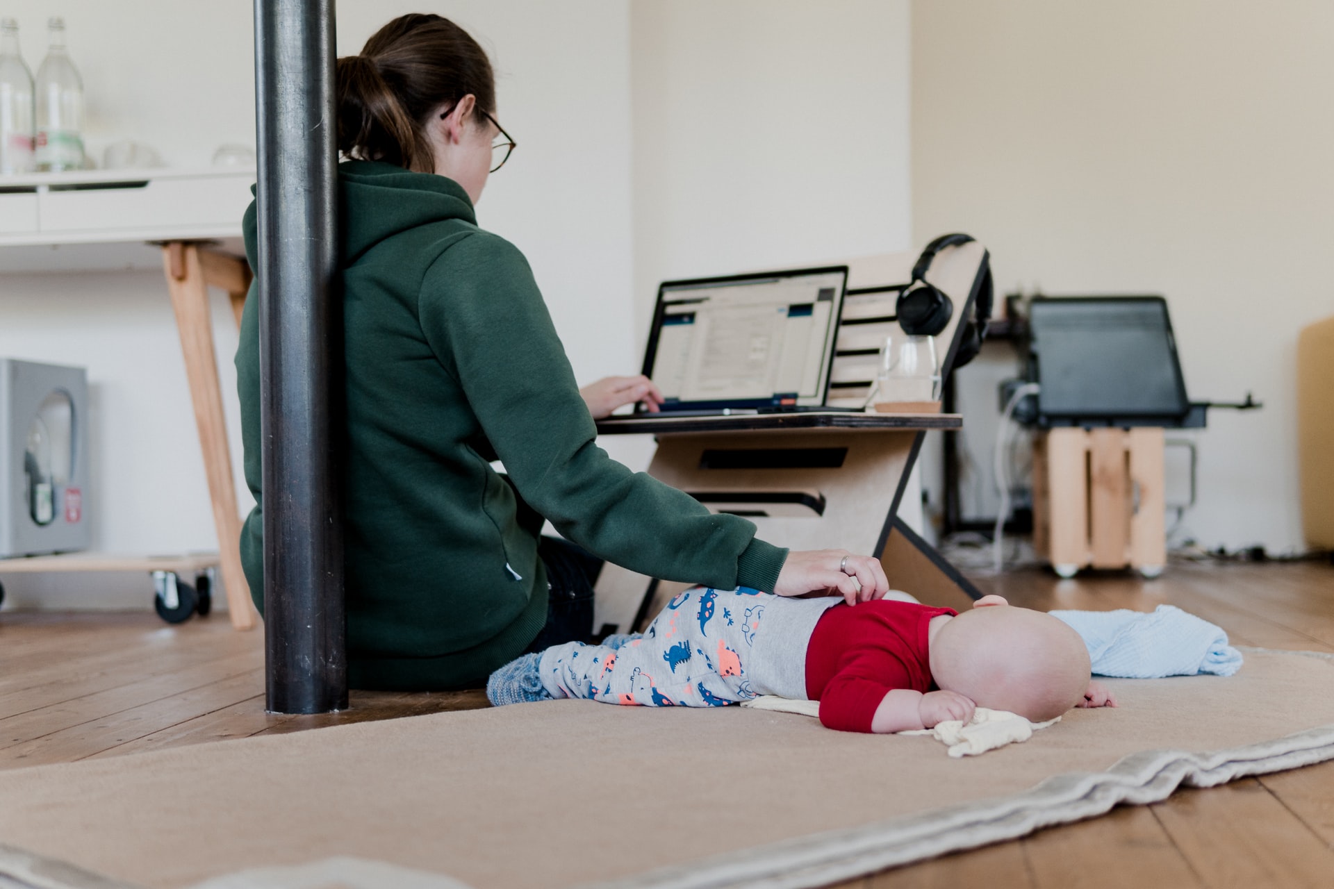 Person sitter på golvet med datorn och en hand på ett spädbarn. Foto. 