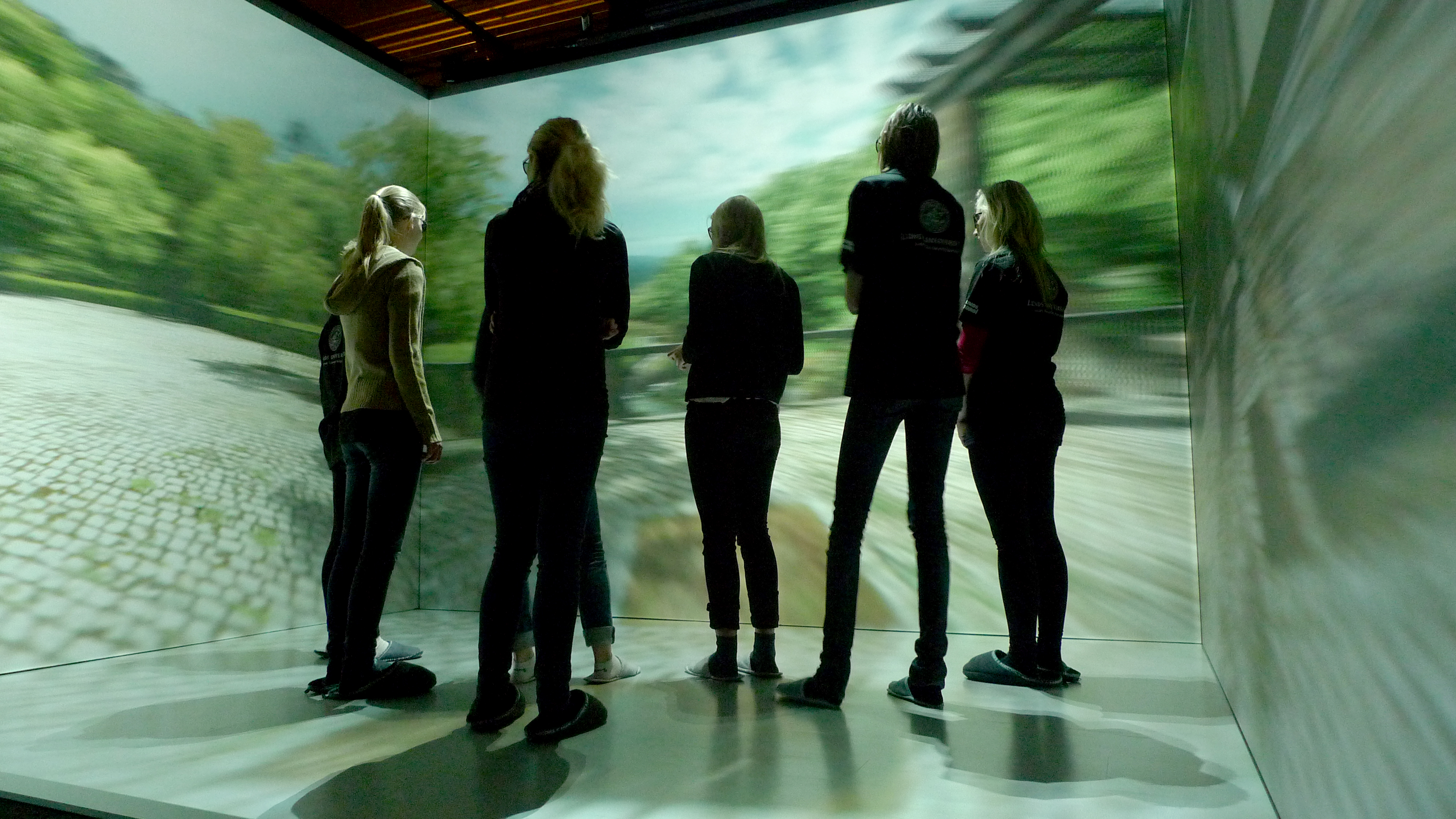 several people standing in a room where a virtual environment is projected at the walls. Photo.