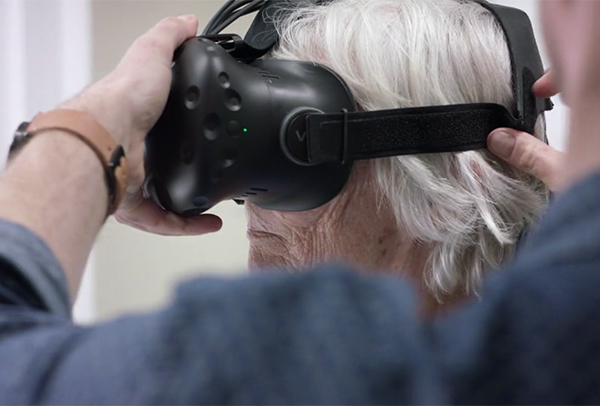 an elderly person has their VR headset adjusted. Photo. 