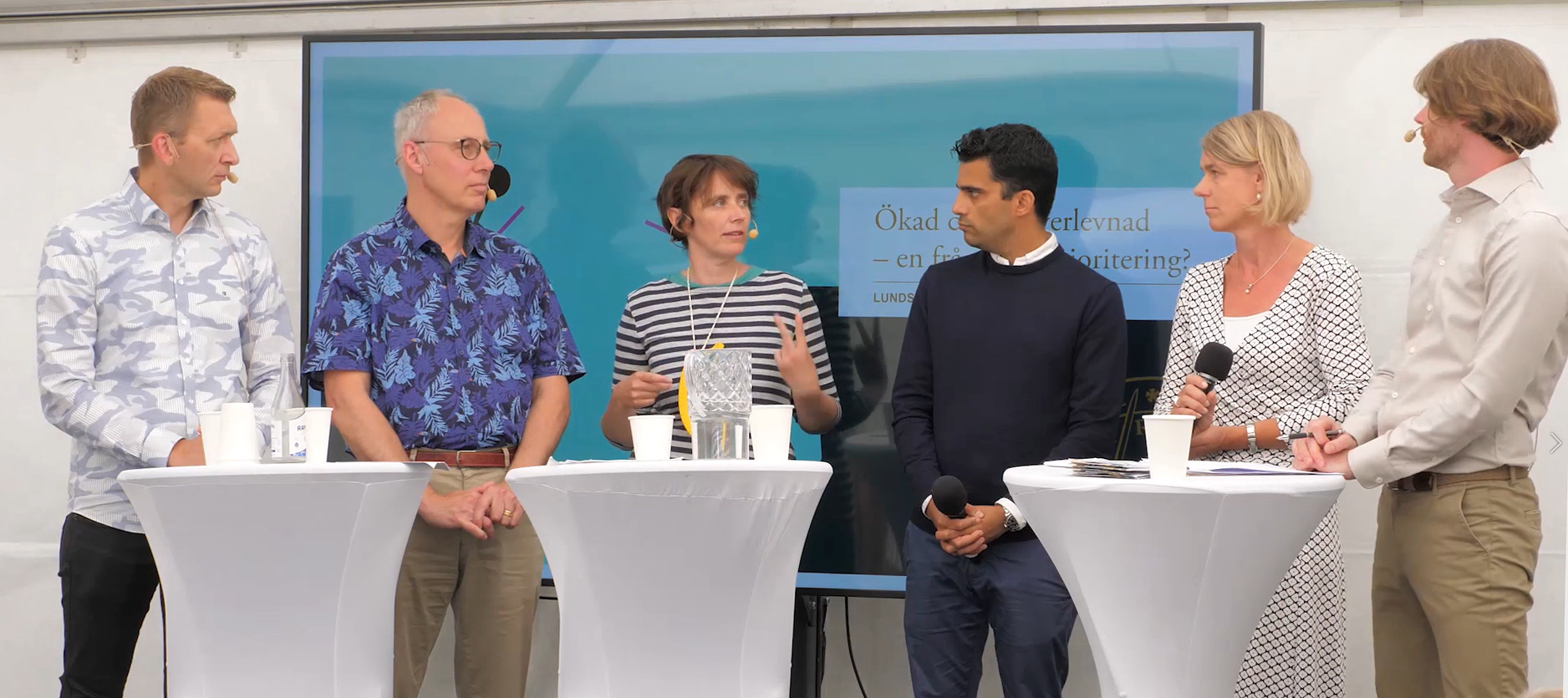 fem personer står på en scen och samtalar. Foto.