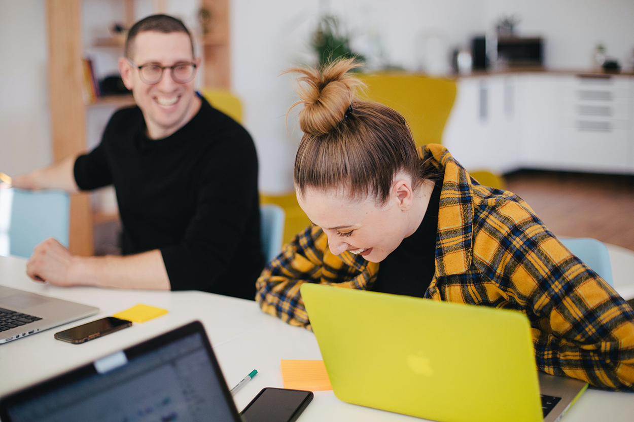 Two people sitting at a desk, laughing. Photo.