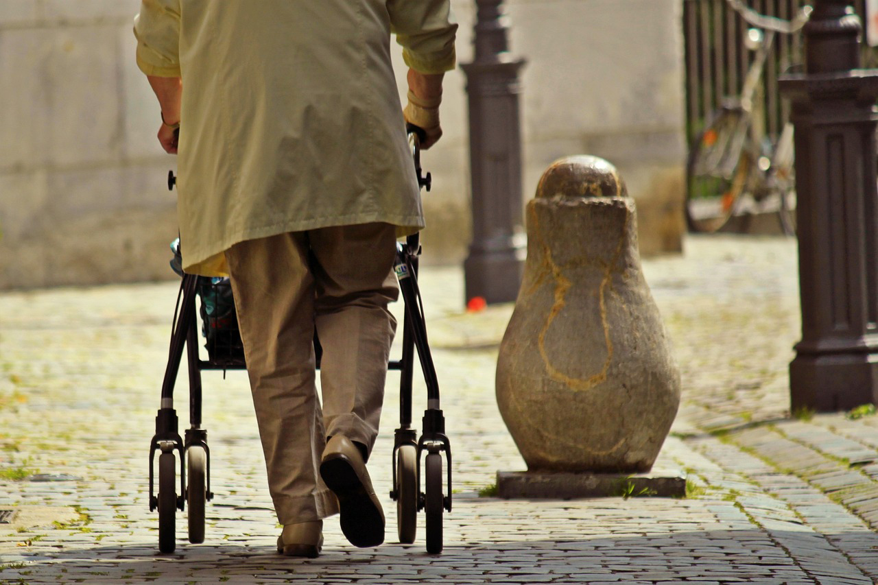 Elderly person walking with a walker on cobblestones. Photo.